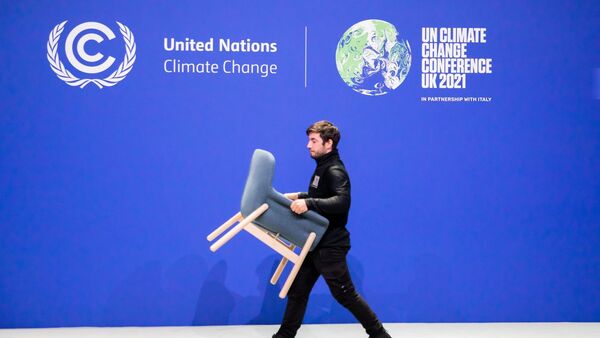 Ein Mitarbeiter trägt bei der UN-Klimakonferenz COP26 einen Stuhl von einer Bühne., © Christoph Soeder/dpa