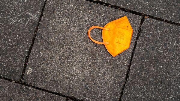 Ein gebrauchter orangefarbener Mund-Nasen-Schutz liegt auf dem Gehweg., © Peter Kneffel/dpa/Symbolbild